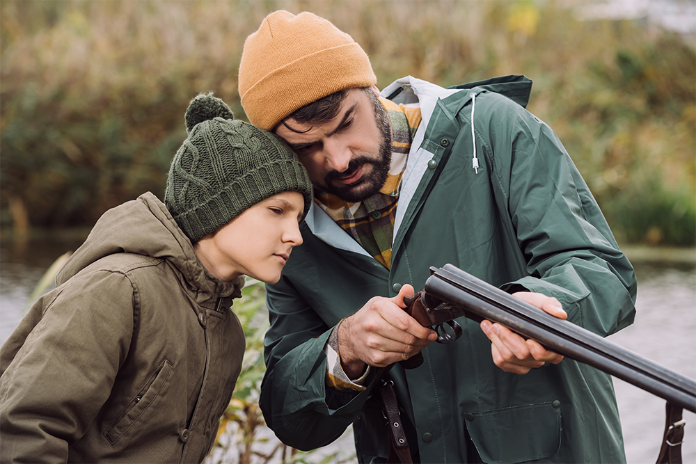 Un chasseur expérimenté montre la vérification de chargement d'un fusil de chasse à un jeune accompagnant.