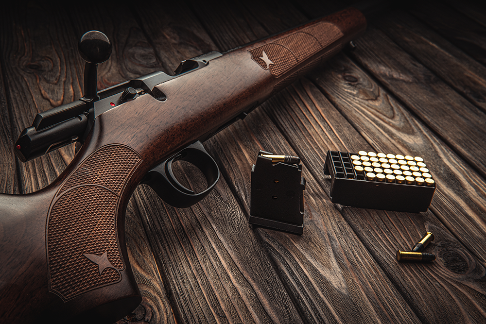 Carabine à verrou calibre .22 LR avec finition bois, accompagnée d’un chargeur, d’une boîte de munitions et de cartouches sur table en bois, idéale pour le tir sportif de précision