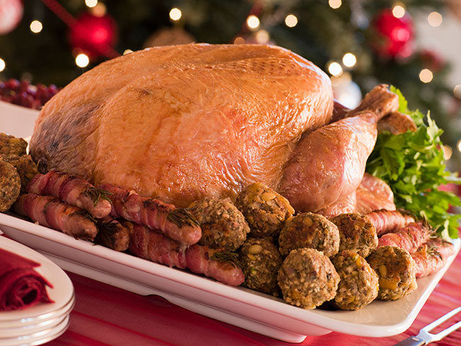 Dinde rôtie entourée de bouchées festives et de légumes, présentée pour un repas de Noël.